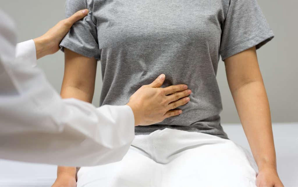 Imagem de um doutor examinando a parte da barriga de um paciente vestido com blusa cinza e calça branca